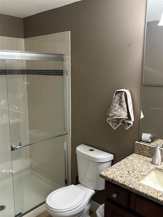 full bath with a stall shower, a textured ceiling, toilet, vanity, and a textured wall