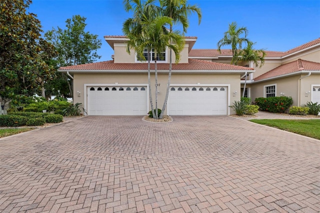 view of front of home featuring a tiled roof, an attached garage, decorative driveway, and stucco siding