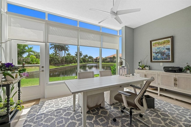 office space with a water view, a ceiling fan, a textured wall, a textured ceiling, and light tile patterned flooring
