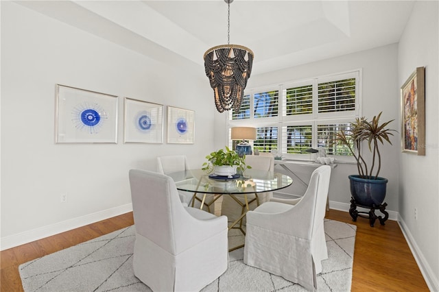 dining area with a chandelier, wood finished floors, baseboards, and a tray ceiling