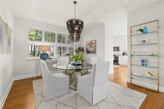 dining space featuring light wood finished floors, a notable chandelier, baseboards, and a raised ceiling