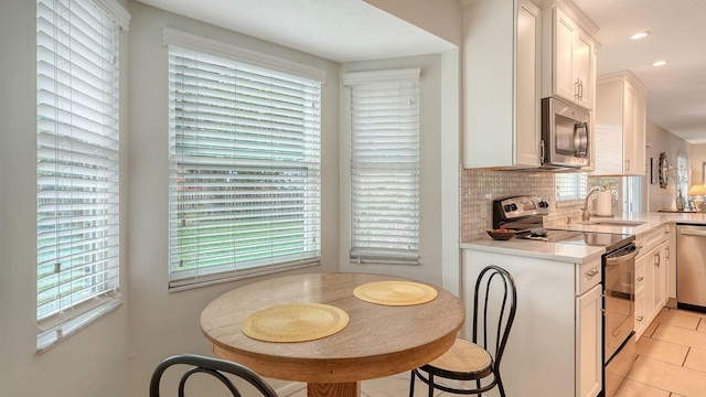 kitchen with light tile patterned floors, light countertops, a sink, stainless steel appliances, and decorative backsplash