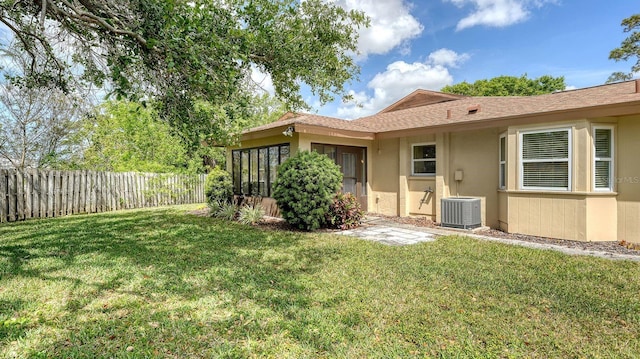 back of property featuring stucco siding, central AC, fence, and a lawn