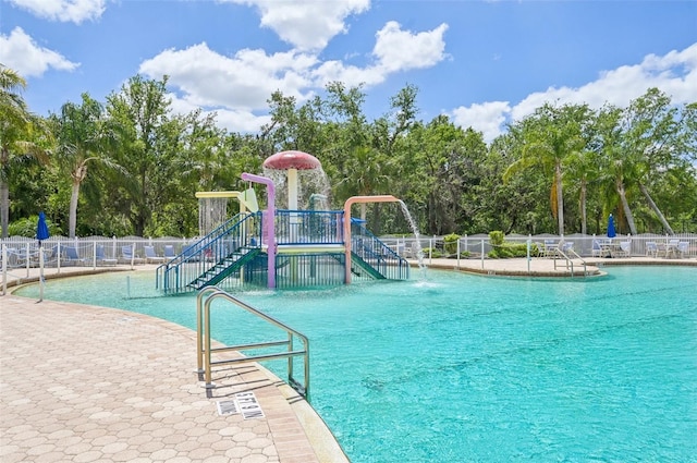 view of swimming pool featuring a water play area, fence, and playground community
