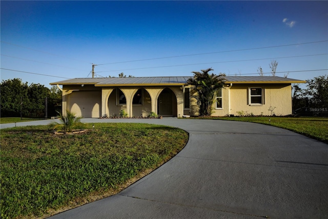 ranch-style house featuring a front yard, curved driveway, an attached garage, and metal roof