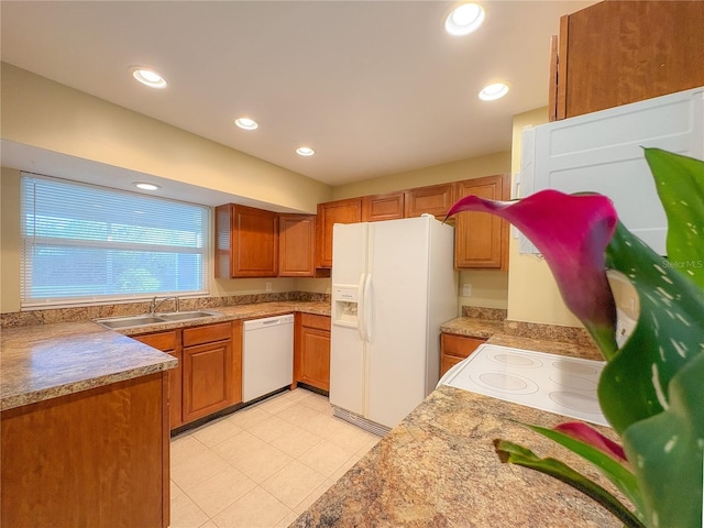 kitchen featuring brown cabinetry, a sink, white appliances, and recessed lighting