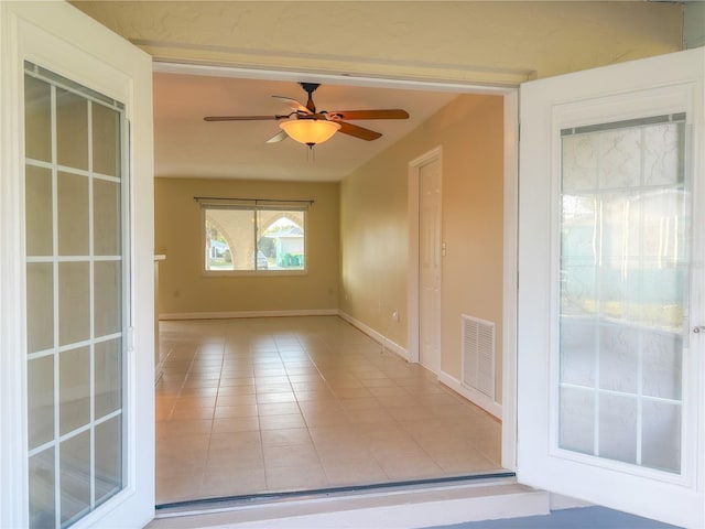 empty room featuring tile patterned flooring, visible vents, baseboards, and a ceiling fan