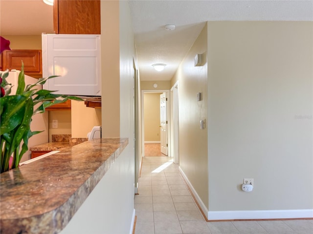 hall featuring baseboards, a textured ceiling, and light tile patterned flooring