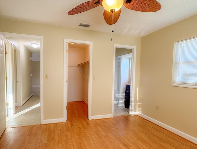 unfurnished bedroom featuring a closet, light wood-type flooring, baseboards, a walk in closet, and visible vents