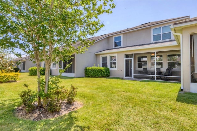 rear view of property featuring stucco siding, a yard, and a sunroom