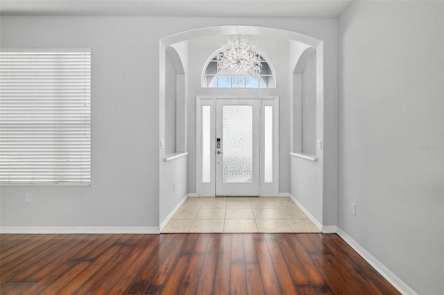foyer entrance with baseboards, arched walkways, wood finished floors, and a notable chandelier