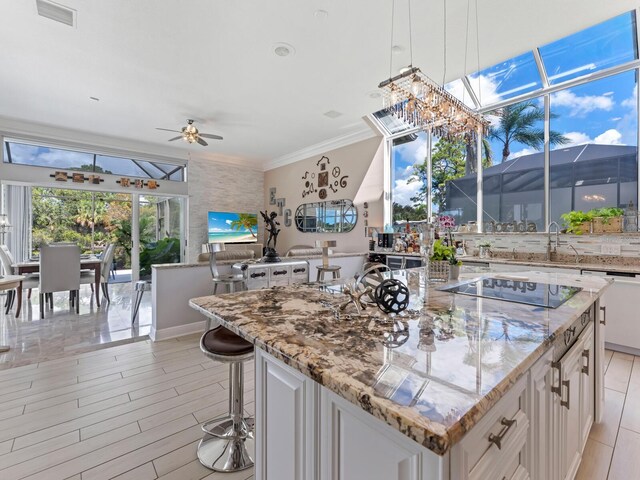 8687 Woodbriar Dr, Sarasota, FL 34238 - kitchen featuring black electric stovetop, a sink, white cabinetry, light stone countertops, and ornamental molding