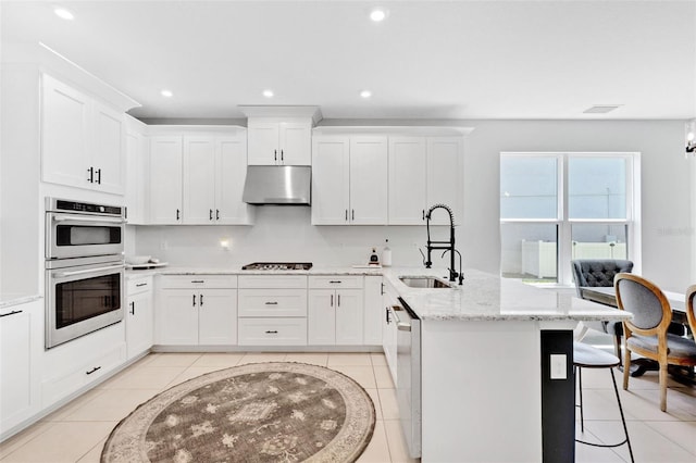 8355 Velda Trl, Sarasota, FL 34241 - kitchen featuring under cabinet range hood, appliances with stainless steel finishes, light tile patterned flooring, a peninsula, and a kitchen breakfast bar
