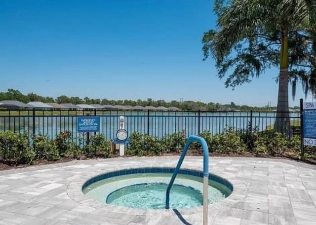 view of swimming pool featuring a water view, fence, and a hot tub