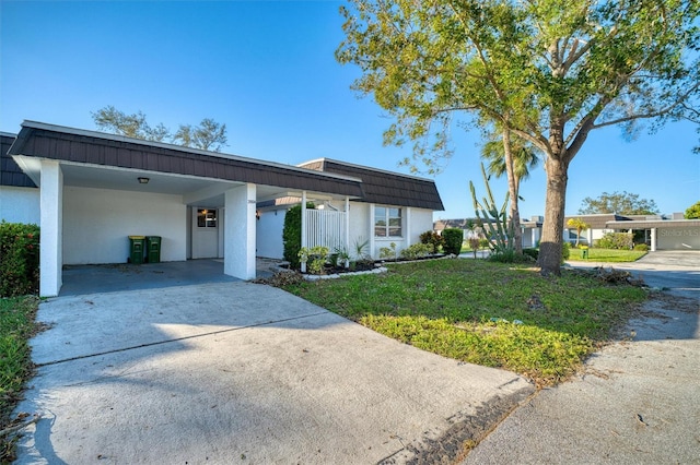 view of front of house featuring mansard roof, driveway, stucco siding, and a front lawn