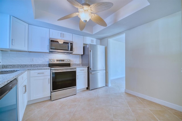 kitchen featuring tasteful backsplash, white cabinets, appliances with stainless steel finishes, a tray ceiling, and light stone counters