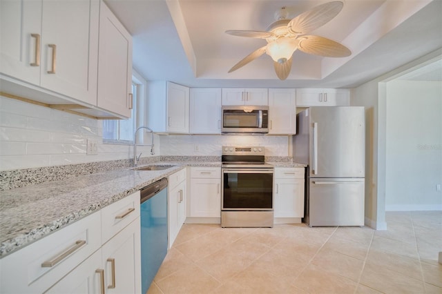 kitchen featuring a tray ceiling, tasteful backsplash, white cabinets, appliances with stainless steel finishes, and a sink