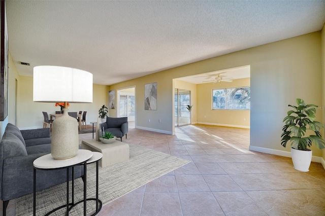 living room featuring baseboards, a textured ceiling, light tile patterned flooring, visible vents, and ceiling fan
