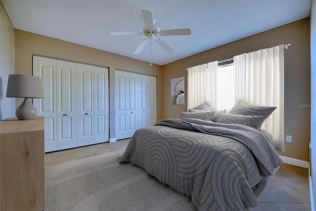 bedroom featuring light tile patterned floors, baseboards, two closets, a ceiling fan, and a textured ceiling