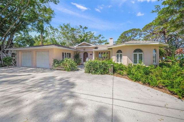 ranch-style house featuring an attached garage, concrete driveway, a chimney, and stucco siding