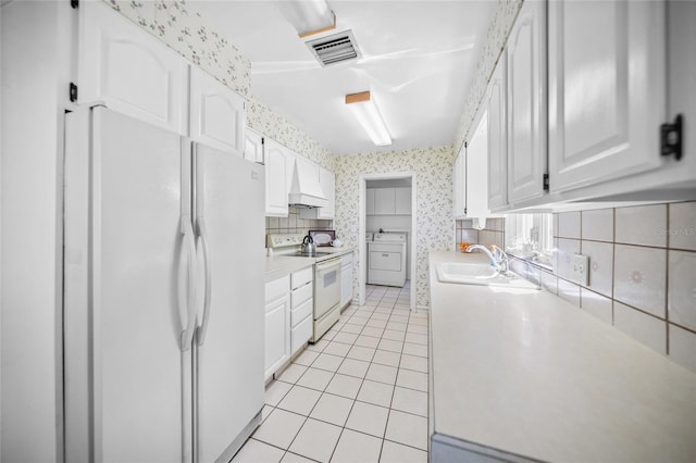 kitchen with a sink, light tile patterned flooring, white appliances, washer / dryer, and light countertops