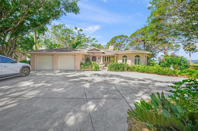 view of front of house with stucco siding, an attached garage, a chimney, and concrete driveway