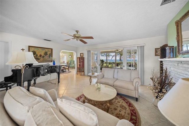 living room with arched walkways, a textured ceiling, visible vents, ceiling fan, and light tile patterned floors