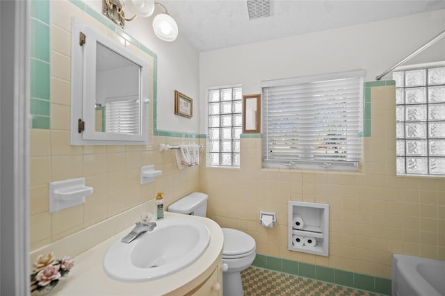 full bathroom with tile patterned floors, a bathtub, toilet, tile walls, and visible vents