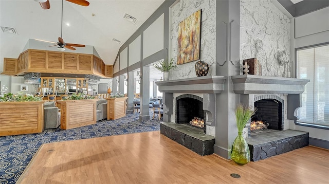 living area with a warm lit fireplace, high vaulted ceiling, a ceiling fan, and wood finished floors