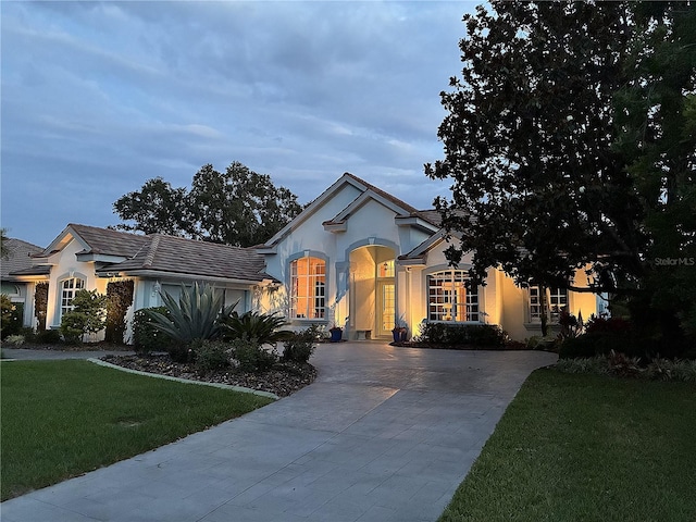 ranch-style house featuring stucco siding, driveway, a front yard, and a tiled roof