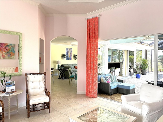 living room with arched walkways, ornamental molding, light tile patterned floors, a ceiling fan, and baseboards
