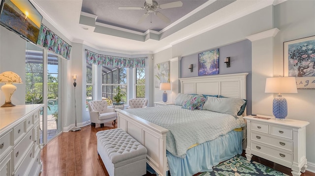 bedroom with access to outside, wood finished floors, a tray ceiling, ornamental molding, and ceiling fan