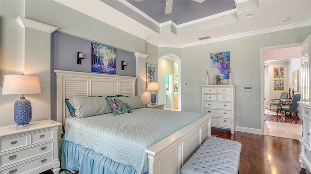 bedroom featuring dark wood-style floors, arched walkways, ornamental molding, a raised ceiling, and baseboards