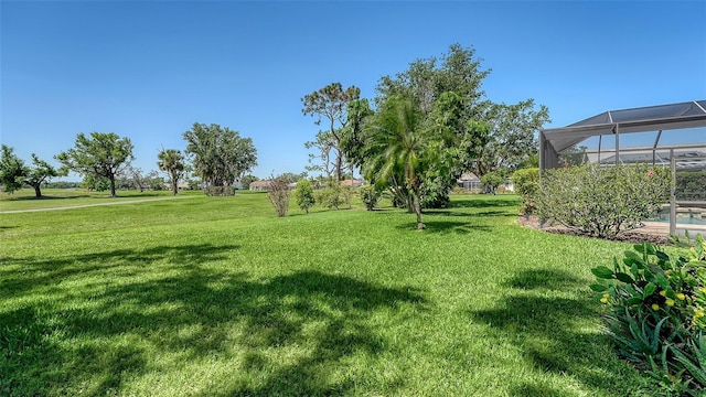 view of grassy yard featuring glass enclosure and a pool