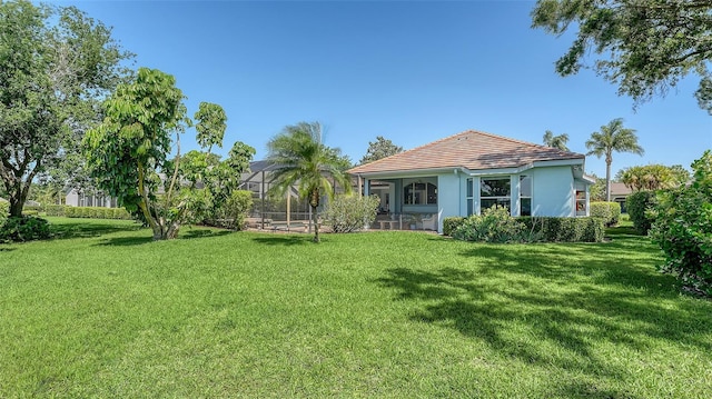 rear view of property featuring a yard, stucco siding, a lanai, and a tile roof