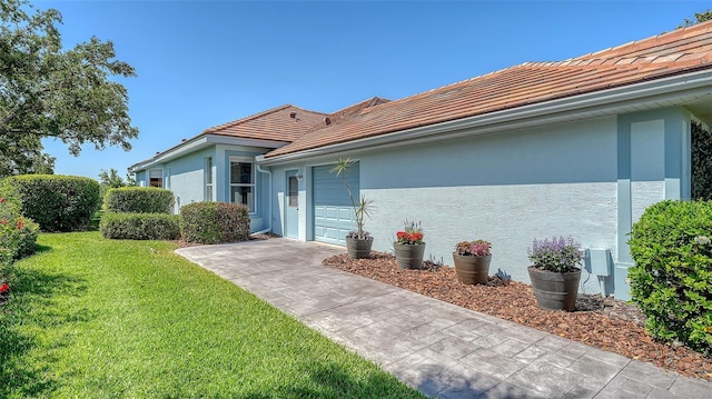 view of side of property featuring a tile roof, stucco siding, a yard, and an attached garage