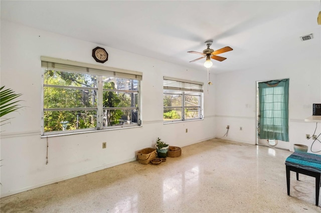 unfurnished room with ceiling fan, visible vents, and speckled floor