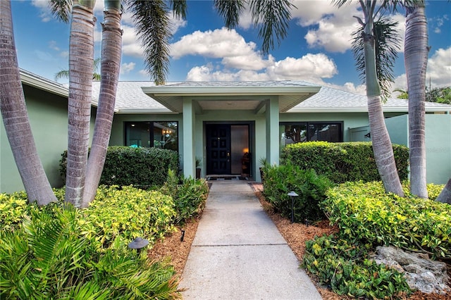 entrance to property featuring a shingled roof and stucco siding