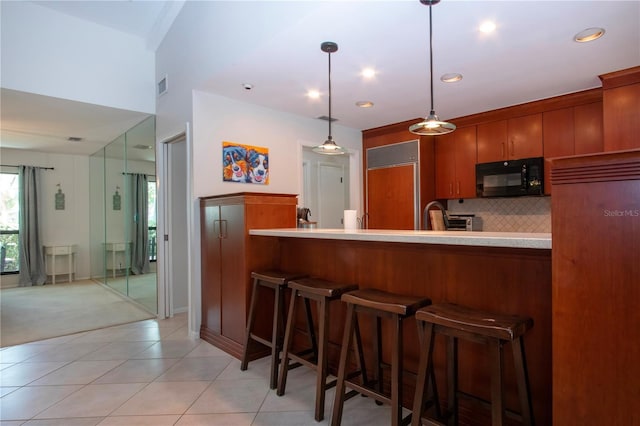 kitchen with black microwave, a kitchen bar, hanging light fixtures, light countertops, and backsplash