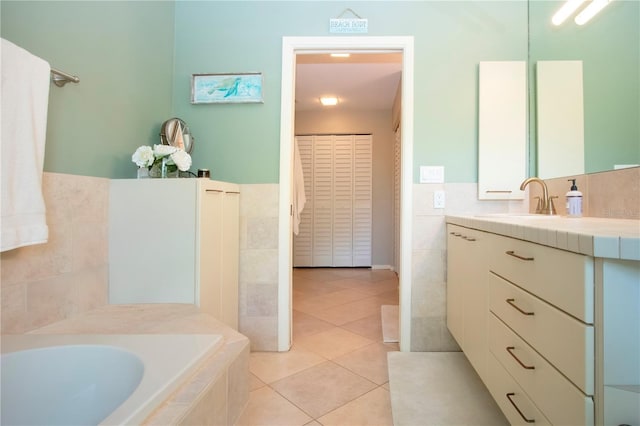 full bath featuring tile walls, tile patterned flooring, vanity, a bath, and a wainscoted wall