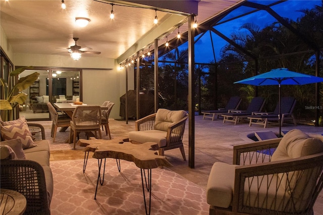 patio at night featuring a ceiling fan, outdoor lounge area, glass enclosure, and outdoor dining area