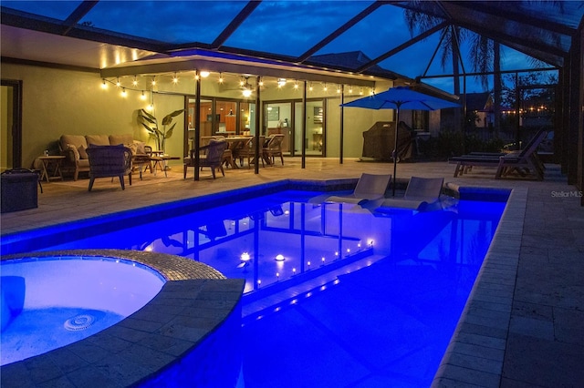 pool at night featuring a pool with connected hot tub, a patio, outdoor dining area, and a lanai
