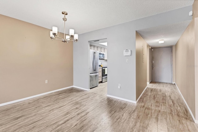 unfurnished dining area featuring light wood-type flooring, a notable chandelier, baseboards, and a textured ceiling
