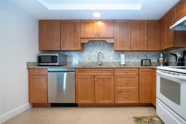 kitchen with stainless steel appliances, tasteful backsplash, a tray ceiling, and brown cabinetry