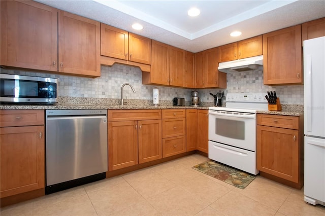 kitchen with brown cabinets, under cabinet range hood, a sink, and stainless steel appliances