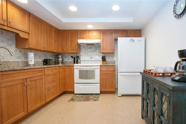 kitchen with a tray ceiling, under cabinet range hood, decorative backsplash, and white appliances