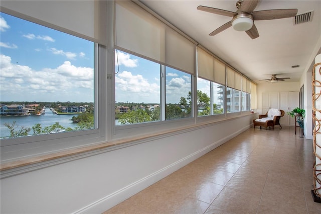 unfurnished sunroom featuring a water view, visible vents, baseboards, and tile patterned floors