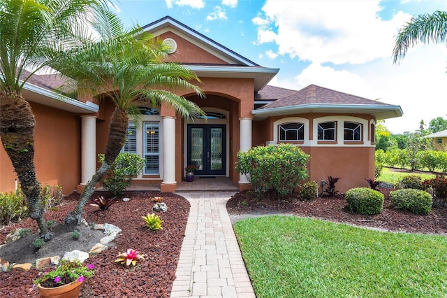 view of exterior entry featuring french doors, a shingled roof, and stucco siding