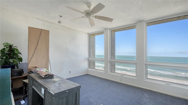 unfurnished office with a textured ceiling, ceiling fan, carpet, and a water view