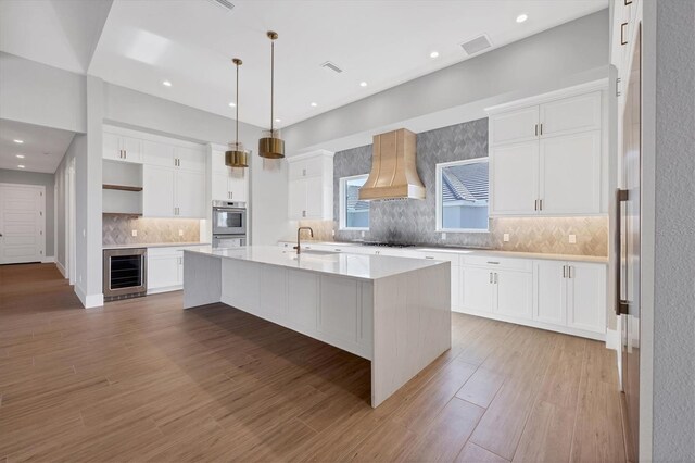 1613 4th St E, Palmetto, FL 34221 - kitchen with beverage cooler, premium range hood, an island with sink, gas cooktop, and light countertops